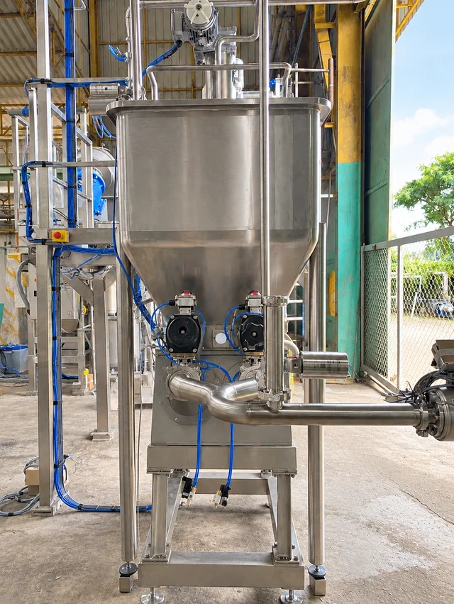 Piston pump with a tall feed hopper and connected pipework.