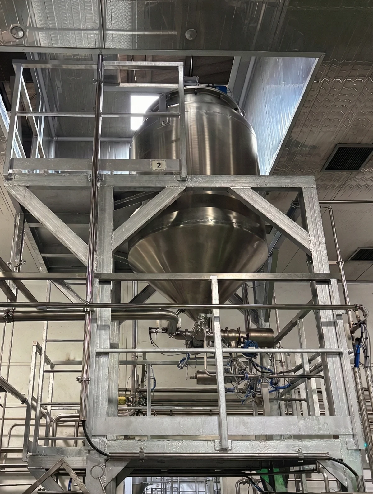 Vertical stainless-steel vessel with its supporting frame and connected pipework.