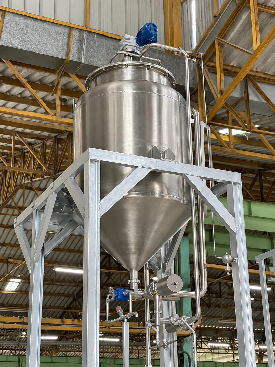 Vertical stainless-steel vessel with a conical base, top-mounted motor, support frame and valves below.