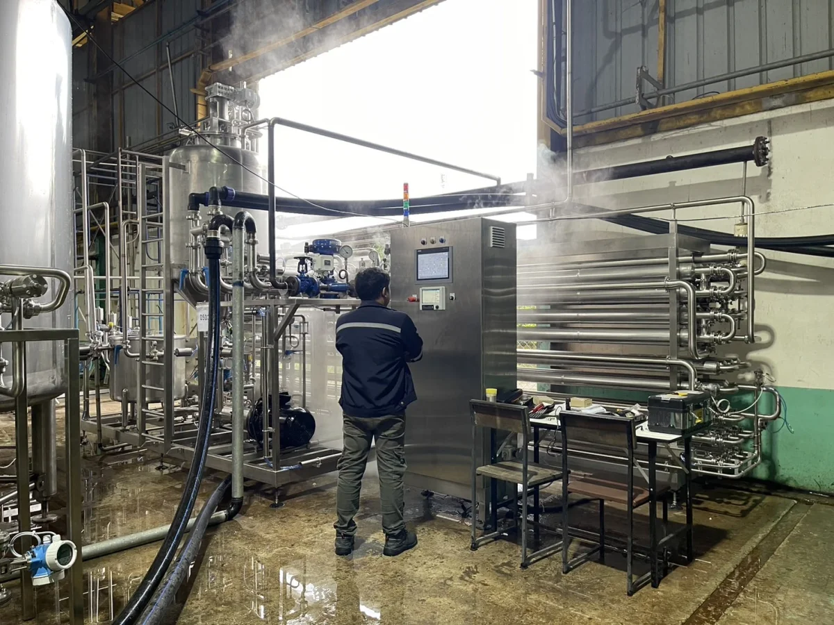 A technician inspecting stainless-steel processing equipment and connected pipework.