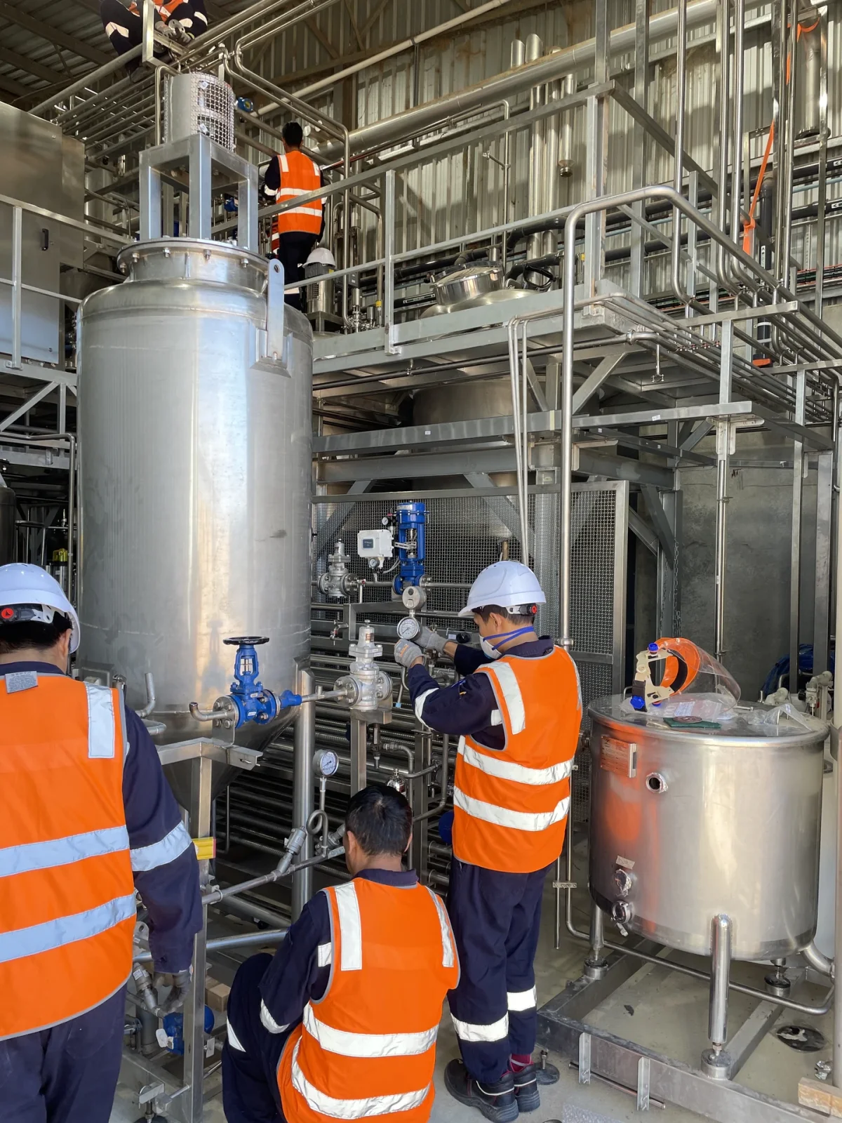 Installation personnel working around stainless-steel tanks and pipework.