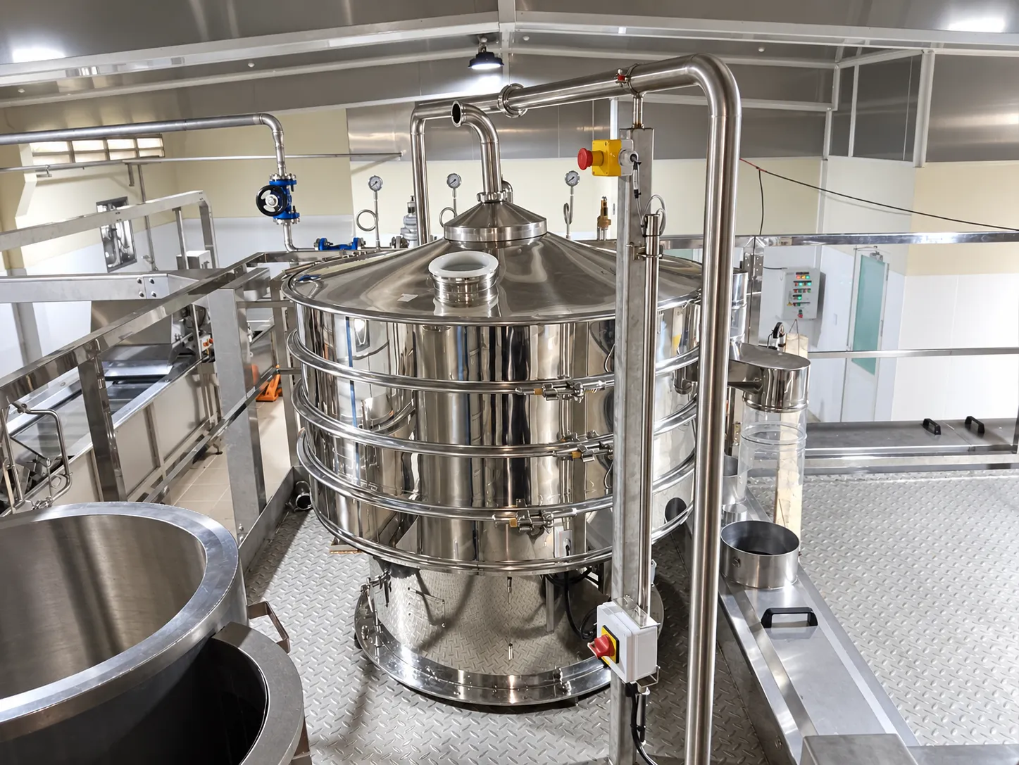 Elevated view of a multi-deck circular stainless-steel screen with nearby pipes and valves.