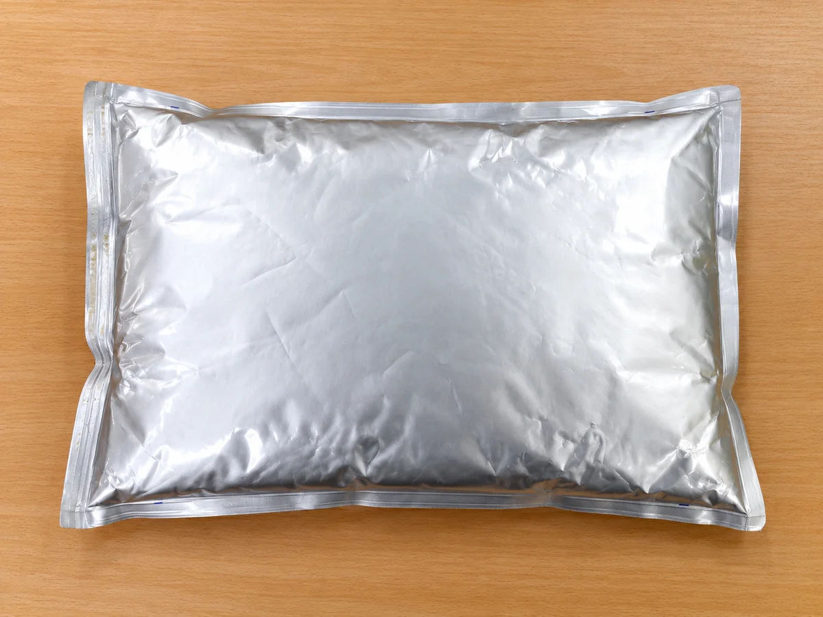 A sealed rectangular silver-coloured pouch resting on a wooden surface.