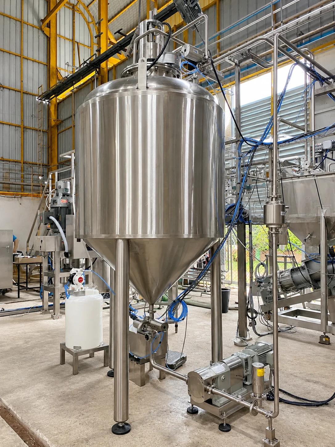 Stainless-steel tank with a top-mounted drive, conical base and transfer pumps.