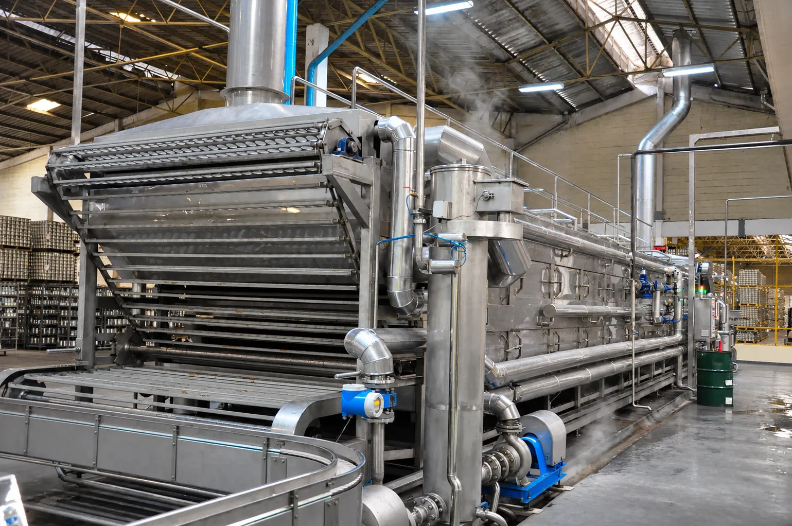Stainless-steel processing equipment with a slatted conveyor, pipework and access railings.