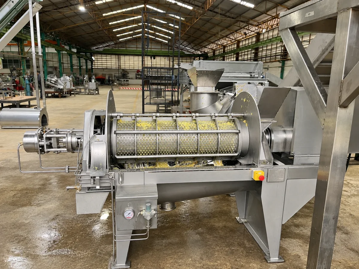 Extraction equipment with a perforated screen and fruit material in the processing area.