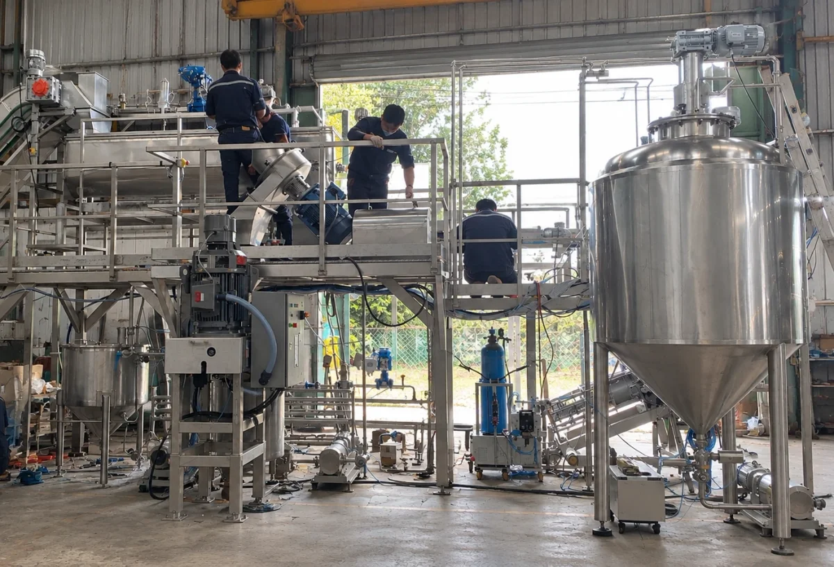 Technicians assembling stainless-steel processing equipment in a workshop.